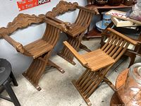 Pair of wooden folding chairs with curved slats, lion head carvings on armrests, ornate carved back rests, and matching folding slatted bench beside them