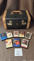 Photo showing the antique McBrine luggage case and 8 Neil Diamond cassette tapes arranged in front.