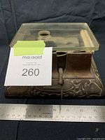 Front view of cast iron base with ornamental design and ruler for scale.