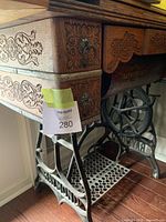 Side close-up of the cabinet showing carved wooden drawers with metal ring pulls and heavy cast iron base with 'Raymond' lettering and ornate design.
