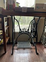 Front view of antique cast iron treadle sewing machine base with decorative metalwork, wooden top, and wheels on one side.