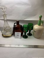 Full view of all six items in the lot showing glass decanter with stopper and gold rim, brown Gooderham & Brown bottle, two green Dom Cafe glasses, and an earthenware rum bottle with green stopper.