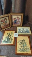 Five framed vintage prints including two Rhonda 3D prints and three Hummel prints on wood, arranged on fabric surface.