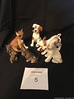 Group photo of six dog figurines including a boxer, a white dog with brown patches on black base, two small darker dogs, and two cream colored dogs on black background.