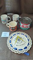 Set of 3 mugs and Melitta Coffee tin with Strachan Freemason decorative plate on fabric surface