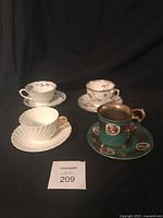 Four bone china cups and saucers grouped together on black background, showing varied decoration styles and colors.