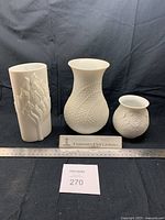 Three white Kaiser Porcelain vases displayed with a scale and a label showing the brand.