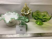 Four vintage glass pieces including two candy dishes with pedestals and two smaller vases, in green and white tones.