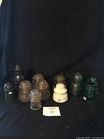 Full collection of 12 vintage insulators displayed against black fabric background showing variety of glass, ceramic, and plastic types