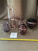 Five purple hue vintage glass vases and urns arranged on fabric background with measuring tape and lot number tag visible