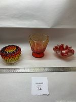 Three vintage glass dishes: a red-yellow footed carnival glass dish with an octagonal rim, a hobnail patterned smaller dish with wavy edges, and a ruffled edge dish, all placed next to a ruler for size reference.