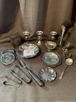 Full view of all silver plated dishes and accessories including candelabra, scallop dish, small bowls, serving utensils, and decorative items.
