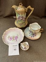 Photo of the full set showing teapot, plate, cup and saucer, mini pitcher and bowl with violet floral designs and gold trim