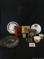 Overall view of the items showing plates, cups, tins, ashtray, and drinking glass together on black background.
