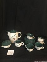 Full set arranged showing coffee pot, creamer, sugar bowl, cups, and saucers against dark background.
