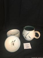 Photo showing 5 bowls stacked and 1 bowl flat with the milk/water pitcher with handle and spout, all decorated with Greenwheat pattern and green rim inside pitcher