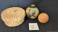 Lot shows all three items side by side on black background: woven basket with lid, smooth stone sphere, and colorful decorative gecko vase.