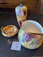 The lot of three antique porcelain pieces displayed on a wooden surface including a Victorian bowl, hand-painted vase and Limoges pitcher.