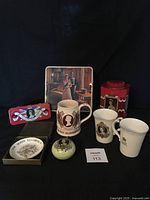 Photo showing metal tins, commemorative mug and dish, ceramic pomander and other Jubilee memorabilia items arranged on black backdrop.