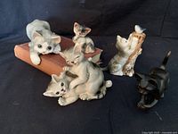 Five cat figurines group photo on black surface, showing all figurines together with brown book