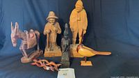 Lot display showing all six carved wooden figures: Thai Buddha, old man with cane, folk art man with poncho, donkey sculpture, painted wooden bird, and wooden puzzle.