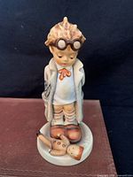 Front view of the Hummel Doctor figurine showing the boy in a white coat with glasses and a fallen doll at his feet.