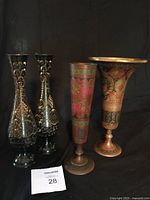 Photo showing four vintage brass vases: two black enameled etched vases and two colorful etched brass vases, all approximately 10 inches tall with detailed floral and geometric engravings.