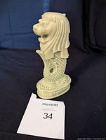 Front left angle view of the light green jade Singapore Merlion statue on black cloth background with item tag 34.