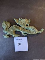 Top-down view of the jade dragon statue showing the full length and detailed carving of scales and features, placed on a dark surface with a lot number card.