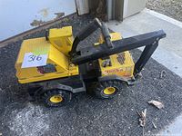 Side view of yellow and black metal Tonka loader truck toy with mechanical arm and bucket on outdoor mat.