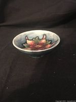 Side angle view of small Moorcroft change dish showing the Columbine flower design and cup shape.
