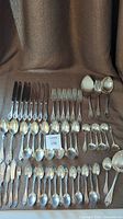 Full set of 55 pieces including knives, forks, spoons, serving utensils laid out on brown fabric.