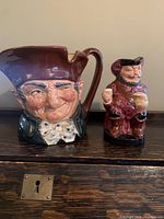 Two Royal Doulton Toby mugs displayed side by side on a wooden surface, showing size and character details.