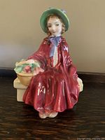 Front angle view of Royal Doulton Linda bone china figurine showing detailed red dress, green hat, and basket of apples.