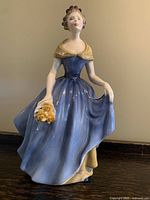 Full view of the Royal Doulton Melanie figurine showing the flowing blue dress and bouquet of yellow roses.