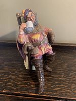 Front angle view of Royal Doulton porcelain figurine showing seated man holding a white beer mug, wearing colorful medieval attire.