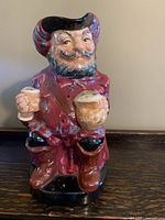 Front and side views of Royal Doulton Toby Mug Sir John Falstaff in a red coat holding two mugs, no visible damage.
