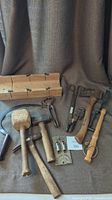 Full view of antique and vintage hand tools including mallets, pliers, wrench, tongs, and thrower arranged on fabric background