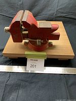 Front and side view of red Sears Craftsman 3-1/2" bench vise mounted on wooden board with ruler for scale.