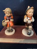 Front view of two Hummel porcelain figurines, School Girl and School Boy, standing on a book.