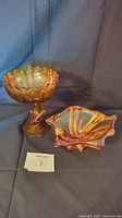 Photo shows two vintage amber glass items—a lotus blossom pedestal bowl and an art glass dish—on dark fabric background.