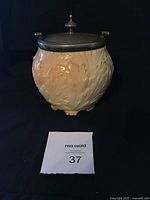Front view of ceramic vintage biscuit barrel with silver plate lid and finial, showing blush ivory floral relief design.