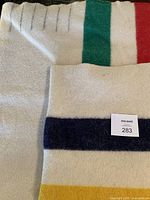 Folded section showing off-white wool and stripes in green, red at top and navy, yellow at bottom, with MacSold sticker label.