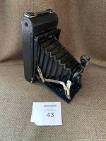 Front angled view of vintage Kodak folding camera with bellows extended and leather carrying case showing wear