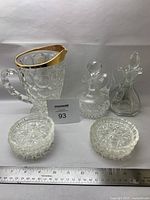 Glass thumbprint pitcher with gold rim, three glass cruets with lids, and six glass coasters arranged together on white surface with ruler to show scale.
