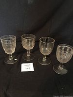 Four vintage pressed glass goblets in a row on black background showing different pressed patterns and shapes.