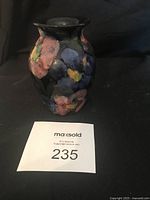 Front view of vintage ceramic vase with brightly painted orchid flowers on dark background.