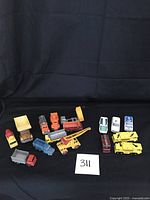 Photo showing all toy vehicles laid out on black cloth background, includes various construction trucks, diggers, dumpers and emergency vehicles.