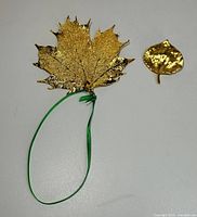 Front view of 10k gold dipped aspen leaf and gold-tone leaf pin on white background
