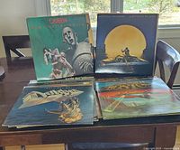 Four vinyl LP covers on table showing Queen News of the World, Jackson Browne Lawyers in Love, unidentified metal-themed cover and spaceship-themed cover